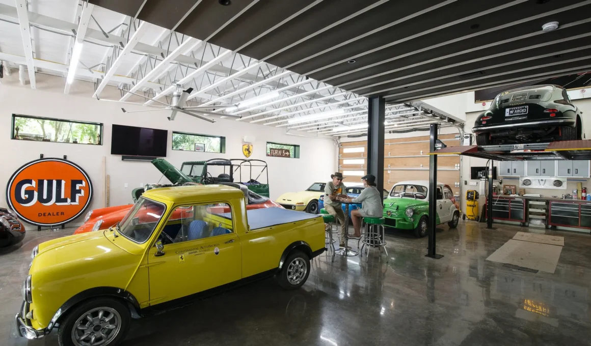 AutoHaus by Matt Fajkus Architecture, interior garage view with exposed steel trusses, vintage car collection, and seating area