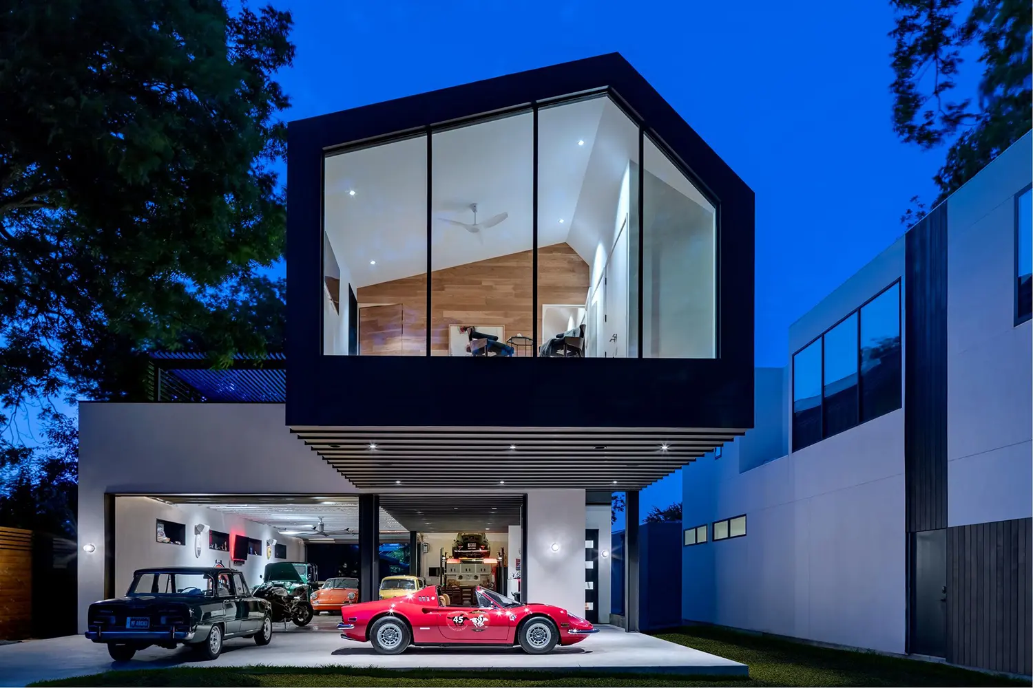 AutoHaus by Matt Fajkus Architecture in Austin, twilight exterior view of cube-shaped upper volume with vintage cars in driveway