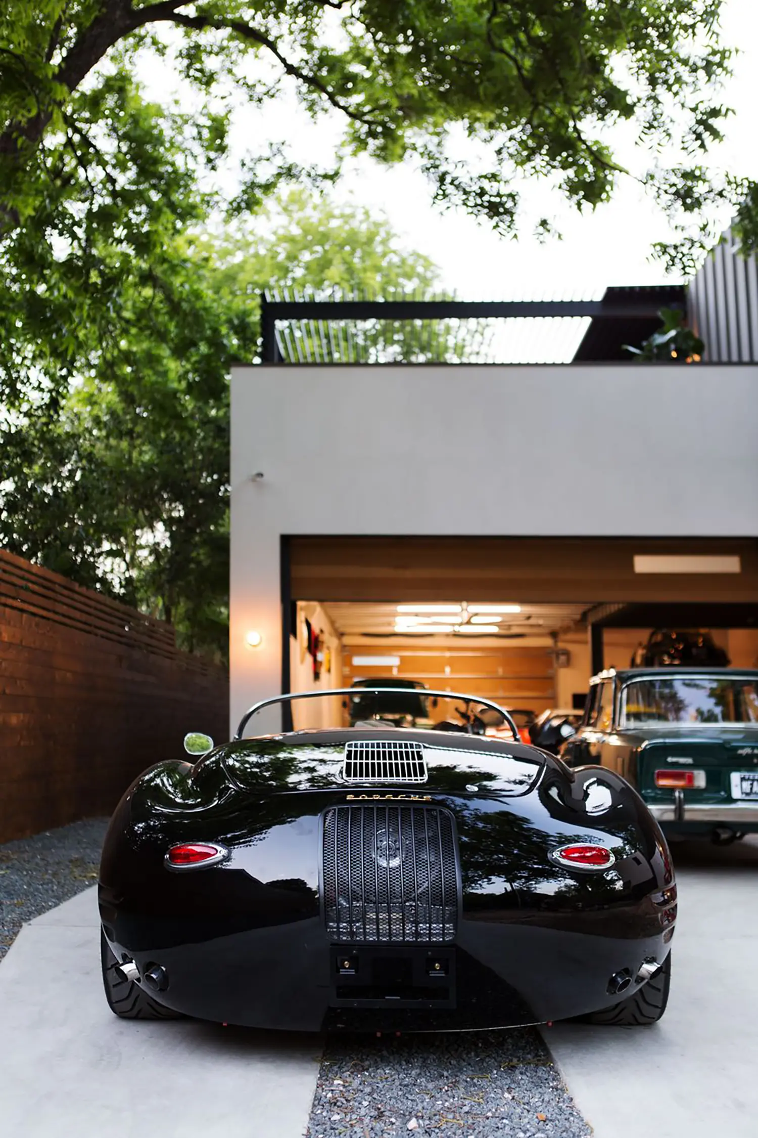 AutoHaus by Matt Fajkus Architecture, vintage black roadster facing open garage entrance at dusk in Austin, Texas