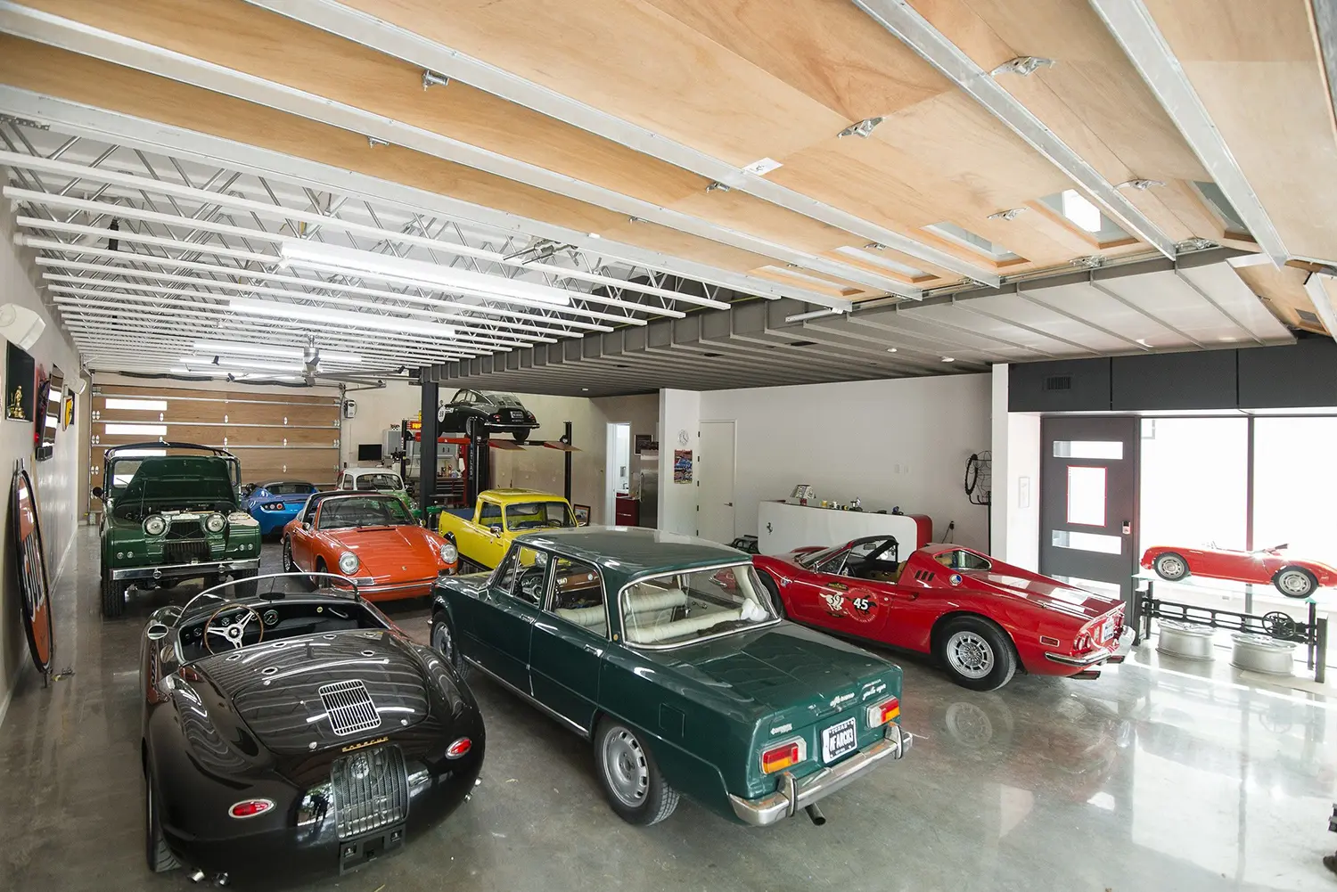 AutoHaus by Matt Fajkus Architecture, wide interior view of garage floor with full vintage car collection and plywood ceiling