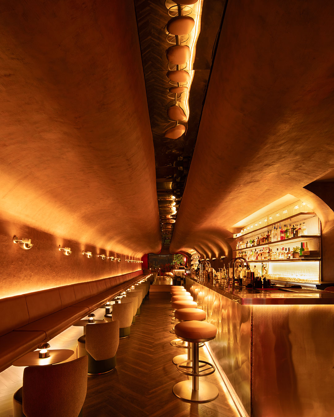 Studiio Dangg introduces a study of industrial contrast and infinite elongation with No Vacancy. The interior is defined by a moody palette where rugged, weathered walls meet the clinical precision of stainless steel. Lighting is used as a tool for spatial sculpting, with concealed coves tracing the soft curves of the volume to highlight the tactile qualities of the corten-inspired surfaces.  Inside, the boundary between performer and guest dissolves. Sage-green stools and leather accents provide a soft, domestic counterpoint to the hard-edged metallic tunnel, creating a concentrated energy reminiscent of a boiler-room setting. It is a curated environment where atmosphere, sound, and liquid mixology converge.  via #urdesignmag 
architects @studiodangg 
images @avesh.gaur  #InteriorArchitecture #NewDelhiDesign #IndustrialChic #HospitalityDesign #StudiioDangg #LightingDesign #Materiality #BarInterior #SonicAtmosphere #ModernDesign #ArchitecturalDetail #Texture