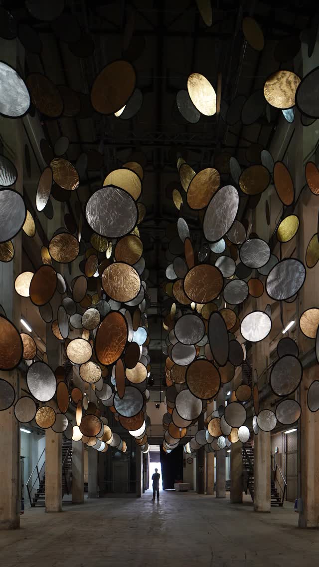 A rhythmic choreography of light defines the encounter with HALOS, where the industrial void of a Florence railway factory is transformed into a celestial landscape. Artist SpY utilizes rotating gold and silver discs to create an ever-evolving field of forms that feels less like a static object and more like a living organism. As the metallic elements overlap and intertwine, they challenge the permanence of the factory’s brick and steel, inviting a contemplative pace where technology disappears in favor of pure poetic effect.  From the ground floor looking up into a suspended sky to the higher galleries overlooking a topographical landscape of light, the installation humanizes the vastness of the site. It serves as a shimmering heartbeat, bringing a temporary, heightened perception to the industrial memory of Florence.  via #urdesignmag
artist @spy__studio 
commissioned by @brightfestival 
images @rubenpb  #SpY #KineticArt #LightInstallation #DigitalArt