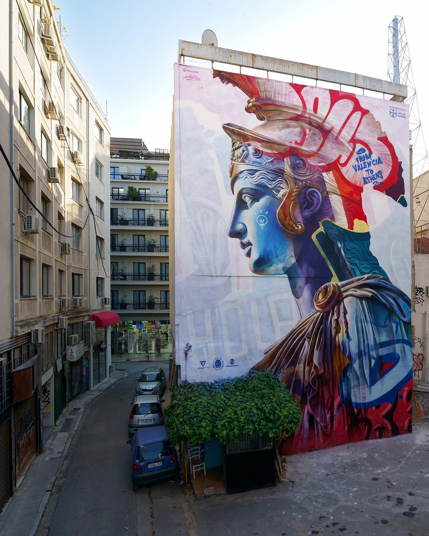 PichiAvo’s debut professional project in Greece, "An Offering to Athens," functions as a cultural bridge where the precision of Hellenistic sculpture meets the raw, energetic pulse of contemporary urban graffiti. Located on Pallados Street, the mural synthesizes the Spanish duo’s signature "urban mythology" with the city’s ancient soul, featuring a multi-layered reimagining of the goddess Athena. The project transforms a standard vertical surface into a vessel for cultural gratitude, ensuring the history of the site remains a continuous, evolving narrative rather than a static relic of the past.  The sensory experience is defined by a striking contrast in texture and hue, where meticulous shading evoking the weight of stone meets the spontaneous, neon-streaked urgency of spray-painted tags. Positioned within sight of the Acropolis, the intervention establishes a visual link that spans millennia, encouraging a re-evaluation of the Mediterranean landscape. From the vibrant blue and red profiles to the intricate layering of light bulb iconography, the work stands as a testament to the power of public art to reconcile the ancient with the immediate.  via #urdesignmag
artists @pichiavo 
images courtesy of PichiAvo  #PichiAvo #AnOfferingToAthens #StreetArtGreece #UrbanMythology #ContemporaryMural