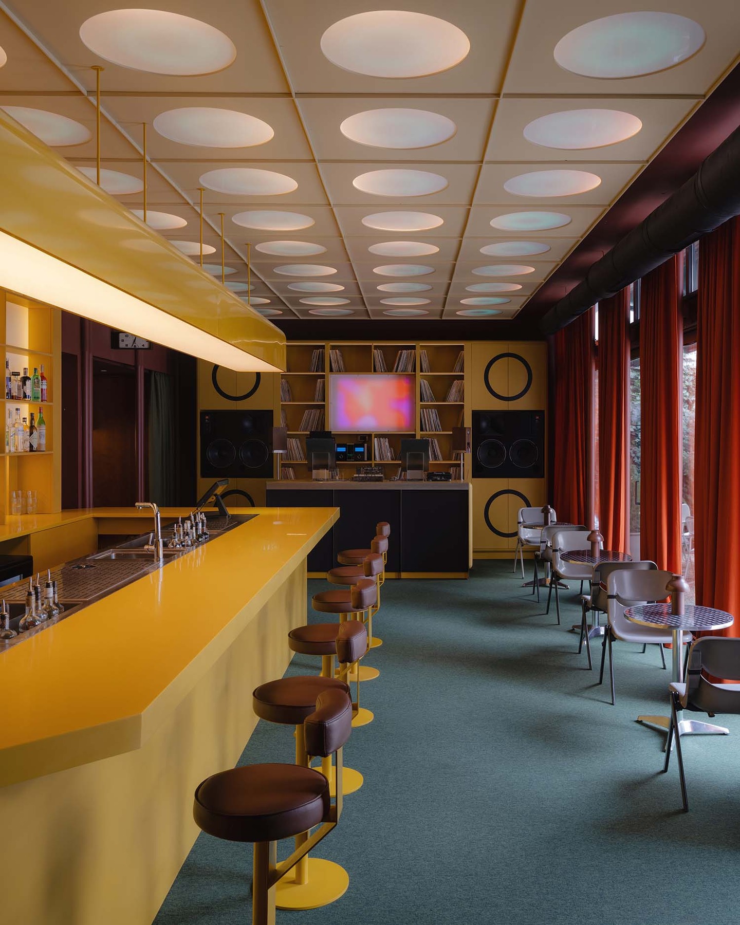 Supaform Studio’s intervention in Belgrade, EJE, functions as a speculative docking station where the modularity of the K67 kiosk meets the ritualistic precision of a Japanese listening bar. The project synthesizes local Yugoslav brutalism with a cinematic, high-fidelity interior, featuring a DJ booth that pays homage to Saša Mächtig’s iconic mid-century design. Every architectural element remains subordinate to the sound, with speakers integrated directly into timber walls and vintage JBL 4435 monitors serving as the venue's analog heart.  The sensory narrative is anchored by custom seating upholstered in original London Underground District line moquette and private Ichiran-style listening booths. This juxtaposition of communal Belgrade energy and introverted Japanese station aesthetics creates a cultural friction that redefines urban hospitality. From the sterile yet comforting glow of oval light panels to the meticulously curated vinyl library, EJE stands as a testament to the power of speculative environments to reshape our perception of the city.  via #urdesignmag
architects @supafrom 
project @eje.belgrade 
images @varvara__top  #SupaformStudio #EJEBelgrade #InteriorDesign #AcousticArchitecture
