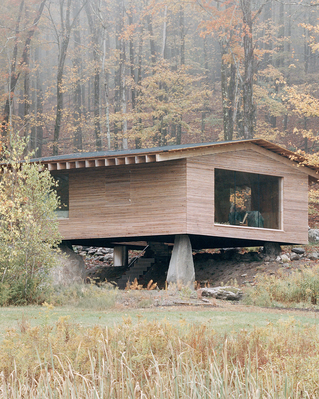 Four glacial boulders, each roughly 500 million years old, support this 91-square-meter larch cabin in Austerlitz, New York, designed by Of Possible as a writing retreat for two Manhattan psychoanalysts. The structure's name, Findling, carries a double meaning in German — "orphan" and "glacial erratic" — both readings load-bearing to the commission. Half the building rests on a New England stone wall likely built between 1770 and 1830, tying the retreat into a continuum of habitation rather than staking a claim to untouched ground. The kitchen island is carved from a single block of Vermont Verde serpentine, quarried from the same source that supplied the planters at Mies van der Rohe's Seagram Building. architects: @of_possible
photography: @arorygardiner urdesignmag.com — link in bio #UpstateArchitecture #CabinDesign #LarchWood #GlacialBoulders #NewYorkRetreat
