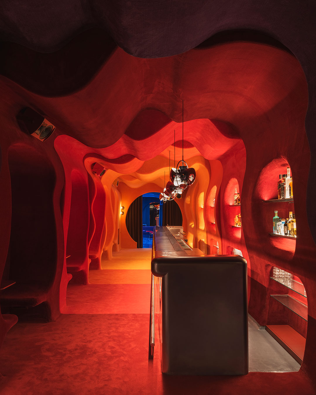 A refrigerator door on a Barcelona focacceria opens into a wall-to-wall carpeted room inspired by Verner Panton's Visiona project — seven color modules from yellow through red to blue, a rounded stainless-steel bar at the center, and organic niches carved into every surface. Isern Serra's Focacha on Carrer Tuset hides what's behind the counter completely. A circular opening leads through to the DJ room, where a domed ceiling with perforated openings shifts light in sync with the music. Two rooms, two registers of the same retro-futurist reference, connected by a threshold that changes the color temperature mid-step. architects: @isernserra
photography: @salvalopez urdesignmag.com — link in bio #Focacha #IsernSerra #barcelonabar #cocktailbar #interiordesign