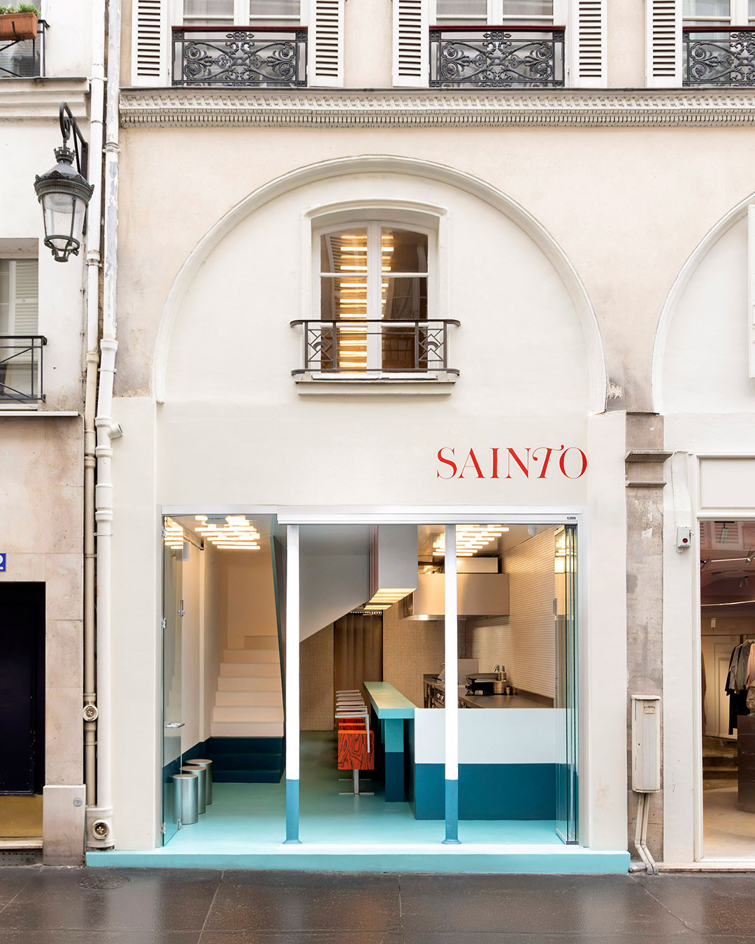 A staircase railing leans against the direction of its own steps — the single most sculptural move inside Sainto, Mur Mur's @sainto_paris Smash Burger restaurant in Paris. Two shades of the same colored concrete render run from ground floor to first floor, turning a fast-food interior into a study in optical depth instead of branding.  Retro American diner references — a long counter, bar stools, a canopy over the bar — get filtered through a minimalist, offbeat logic rather than restaged as pastiche. Red powder-coated tables, stainless steel stools, and a white ceramic mosaic kitchen wall complete the 40 sqm space across two levels.  architects: @mur.mur_architectes
photography: @yvan_moreau_photographe  urdesignmag.com — link in bio  #MurMur #Sainto #ParisRestaurant #InteriorDesign #RestaurantDesign