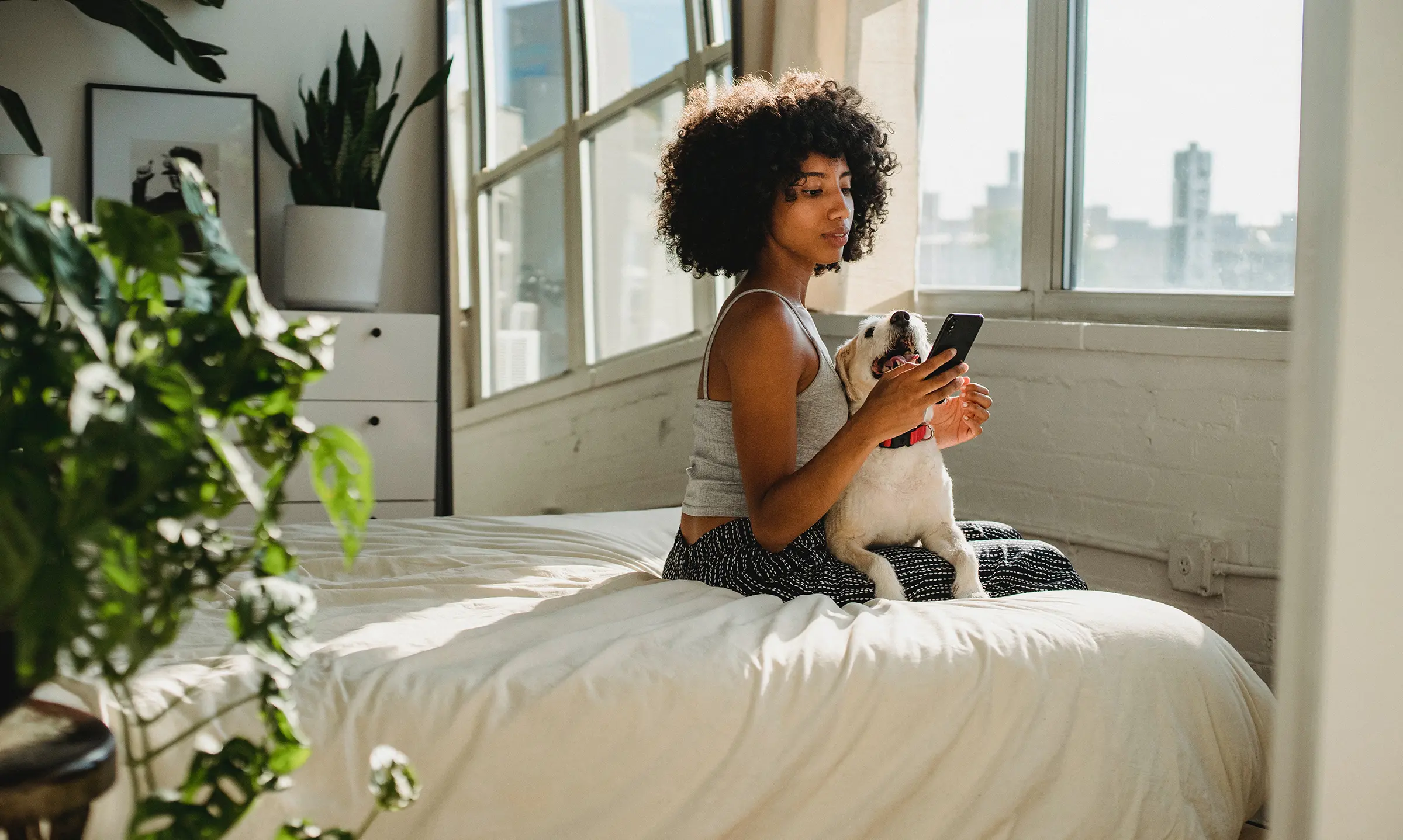 Girl on bed reads message on phone while holding her dog