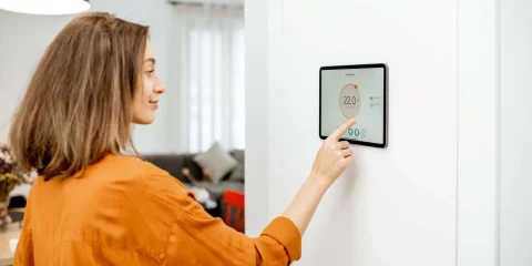 Young woman controlling temperature in the living room with a digital touch screen panel installed on the wall