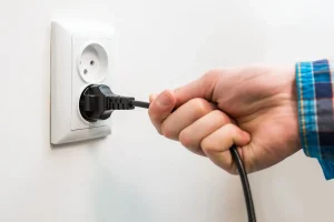 A male hand is pulling an electrical cord plugged into a socket