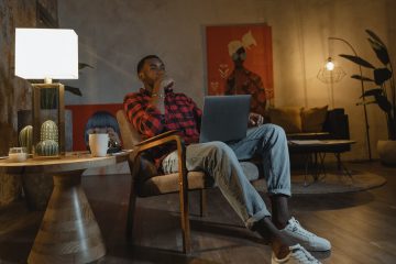 Man surfs online sitting in a chair near a coffee table lit by a table lamp