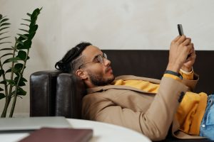 Man watches TikTok on smartphone while lying on a black leather couch