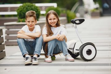 Couple of children sitting near an electric scooter