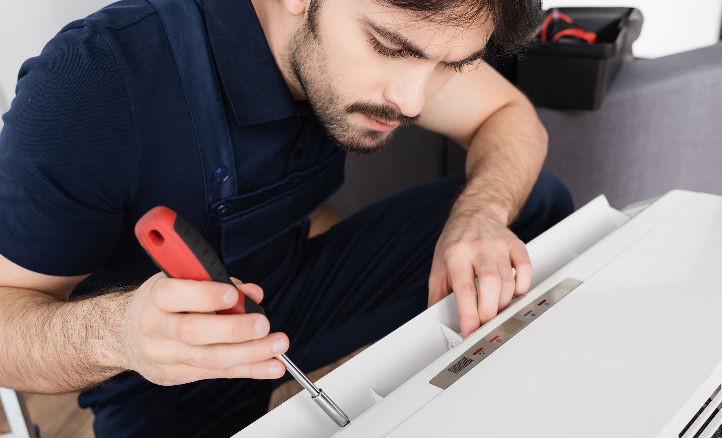 bearded handyman holding screwdriver while fixing modern air conditioner