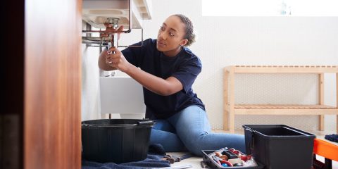 Female Plumber Working To Fix Leaking Sink In Home Bathroom