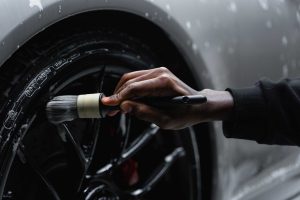 Man's hand holding a brush to clean alloy wheels of a car