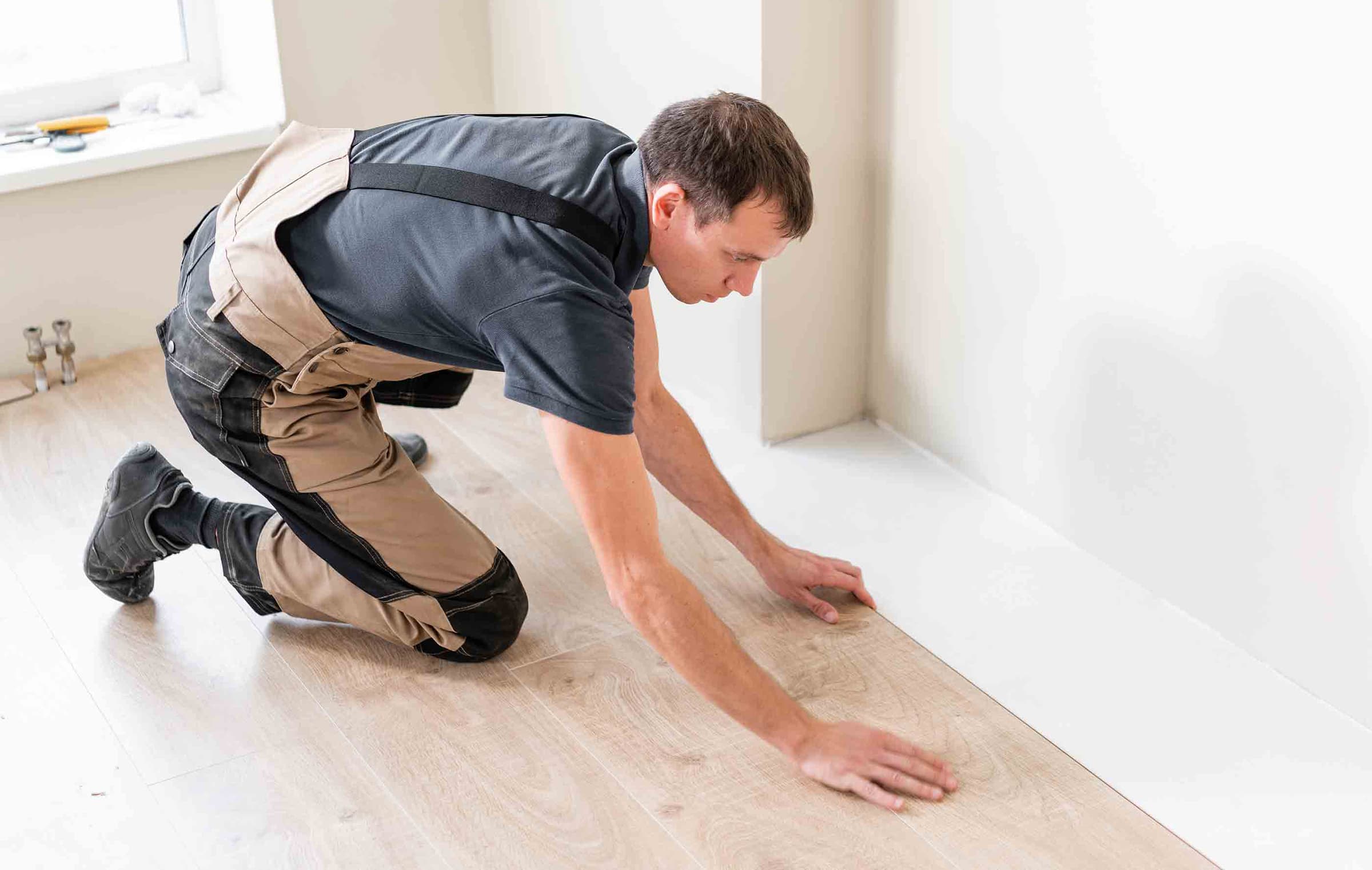 Male worker installing new wooden laminate flooring on a warm film foil floor