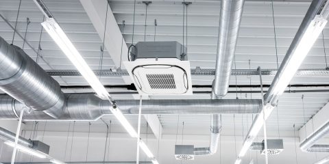 Ceiling mounted cassette type air condition units with other parts of ventilation system (tubes, cables and vents) located inside commercial hall with hanging lights and other construction parts