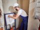 Handsome bearded man in work overalls installing concealed toilet frame in bathroom.
