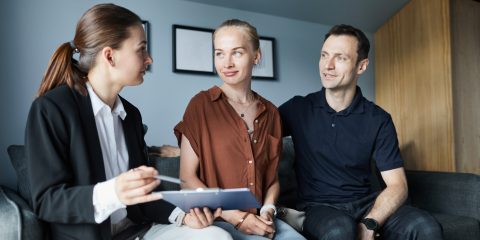 Portrait of female real estate agent signing contract with young couple buying new house