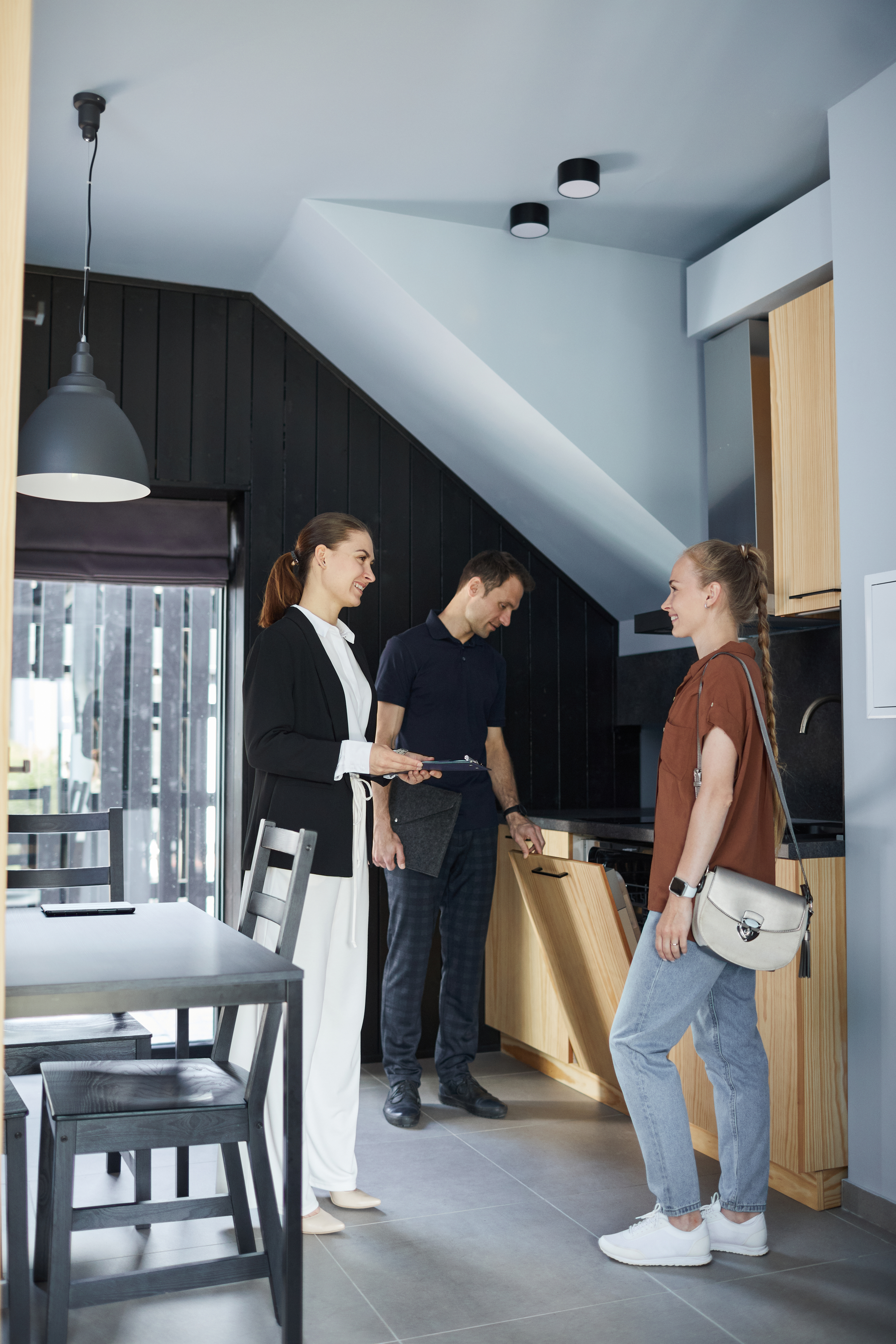 Vertical full length portrait of smiling real estate agent showing house to young couple buying property