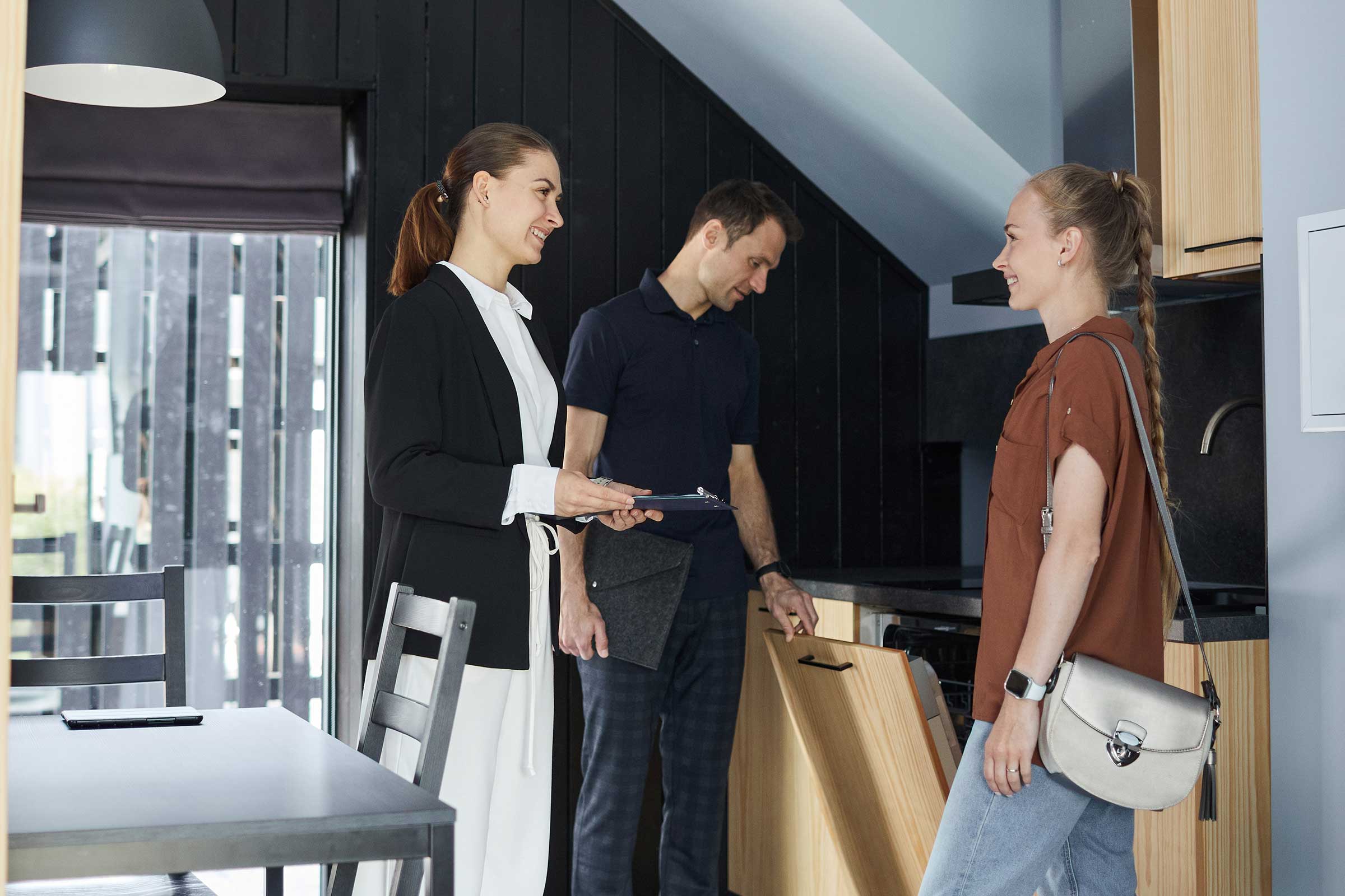 Vertical full length portrait of smiling real estate agent showing house to young couple renting property
