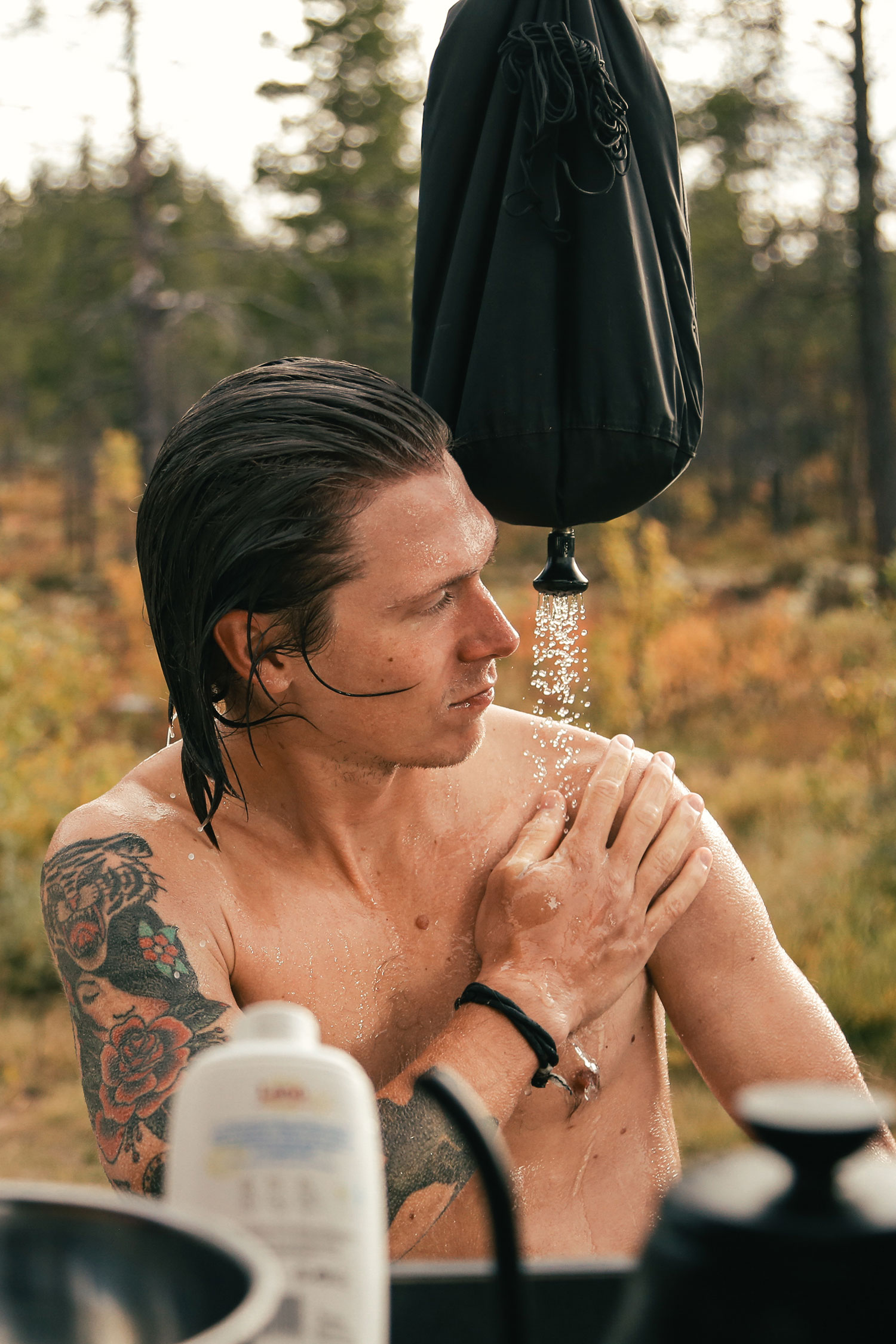 View from inside camper van on young hipster man take shower outdoors from camping pocket shower.