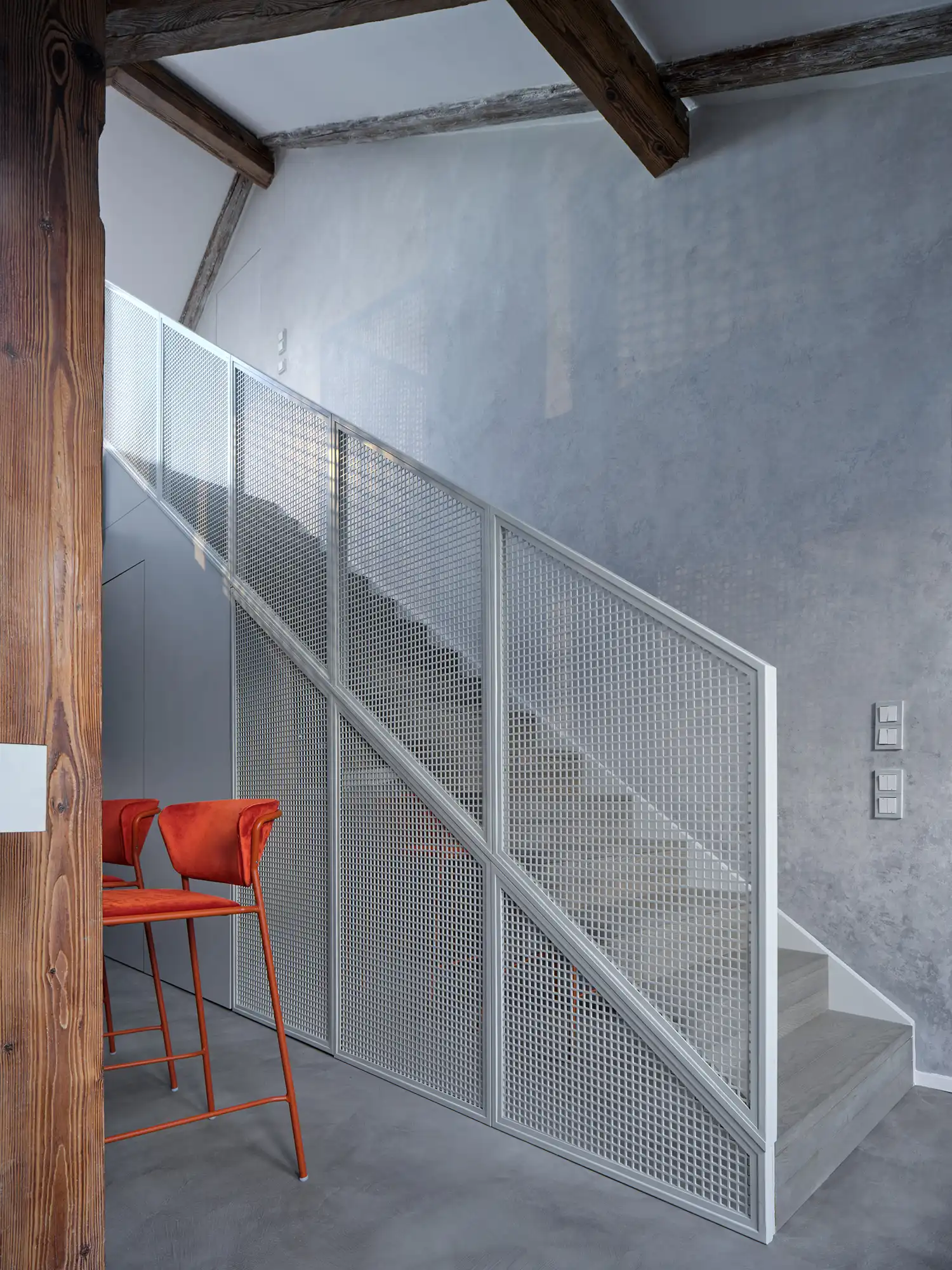 Custom steel staircase in Arbes Square Apartment with perforated metal railings and mirrored base, reflecting the historic Prague attic’s wooden beams.