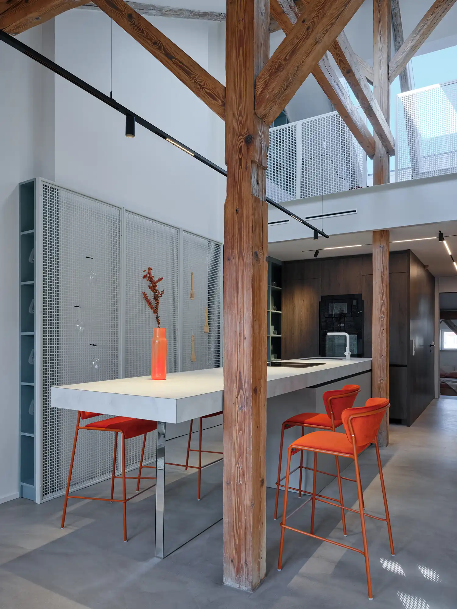 Modern kitchen inside Arbes Square Apartment, featuring matte black cabinetry, terracotta accents, and a perforated steel backsplash under sloped attic ceilings