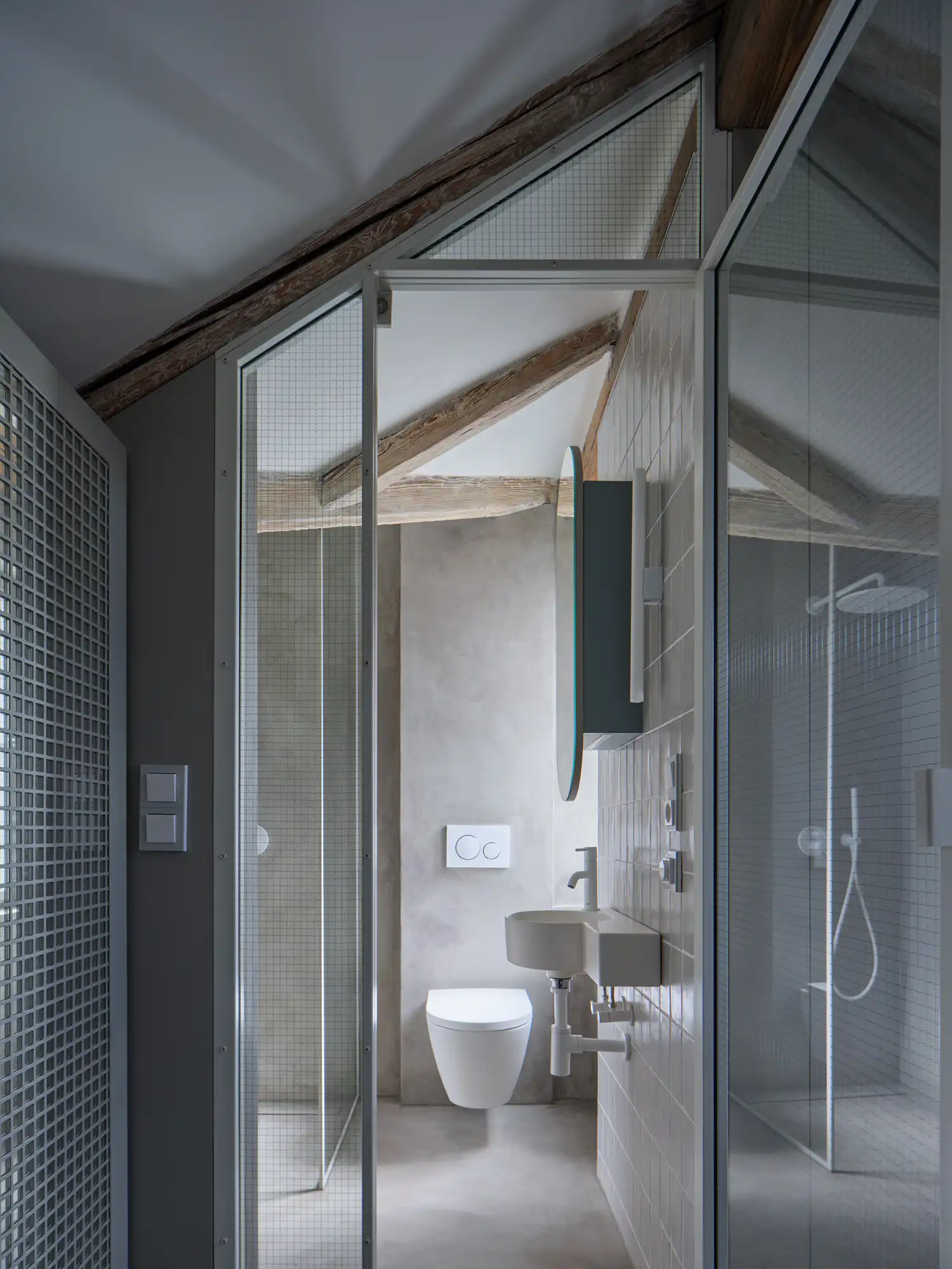 Sleek bathroom in the Arbes Square attic renovation, with matte steel fixtures, pale terrazzo tiles, and a skylight above the shower.