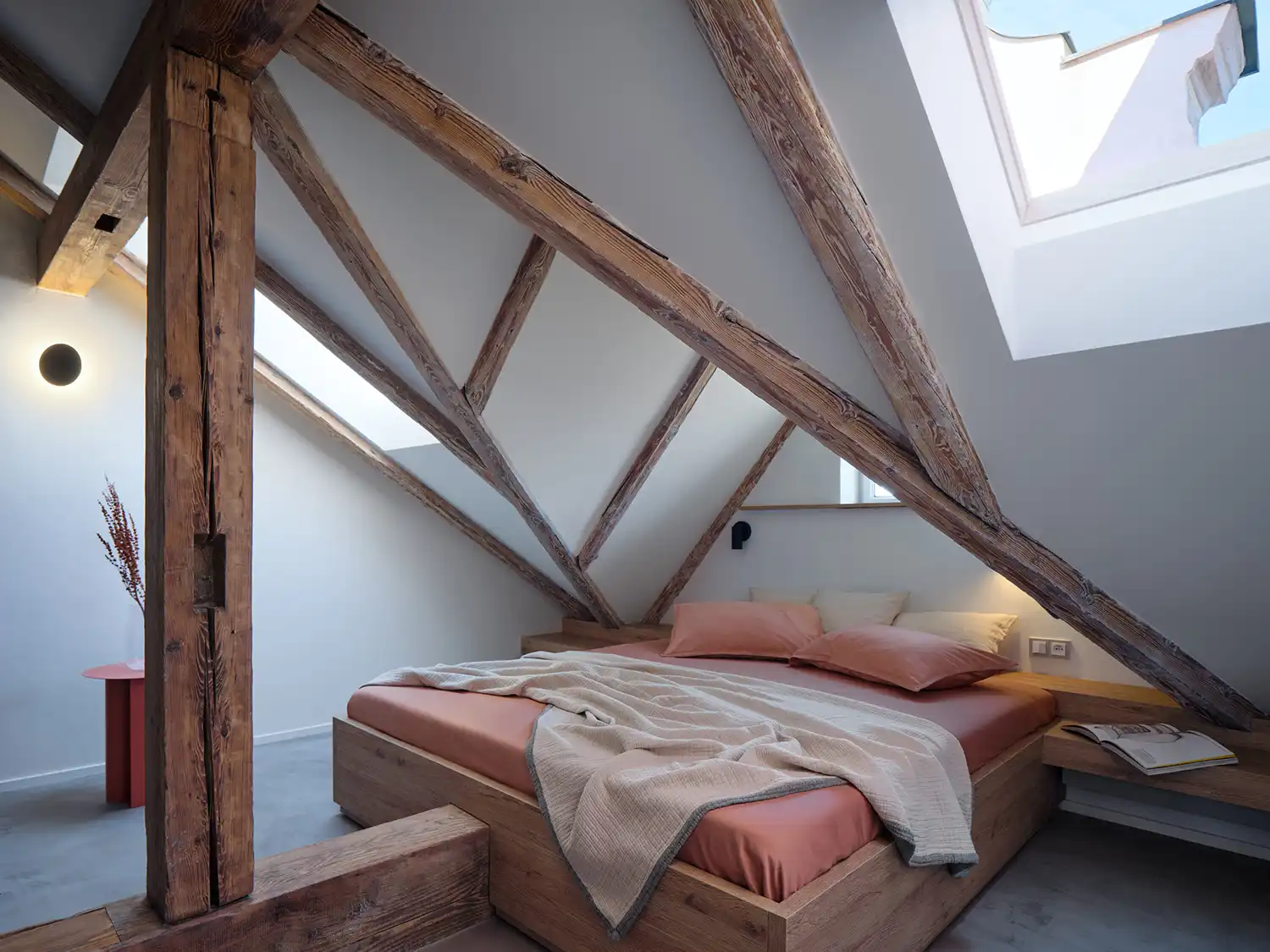 Airy loft bedroom in Formafatal’s Prague apartment, showcasing cream walls, exposed timber rafters, and a minimalist walnut-clad storage block.