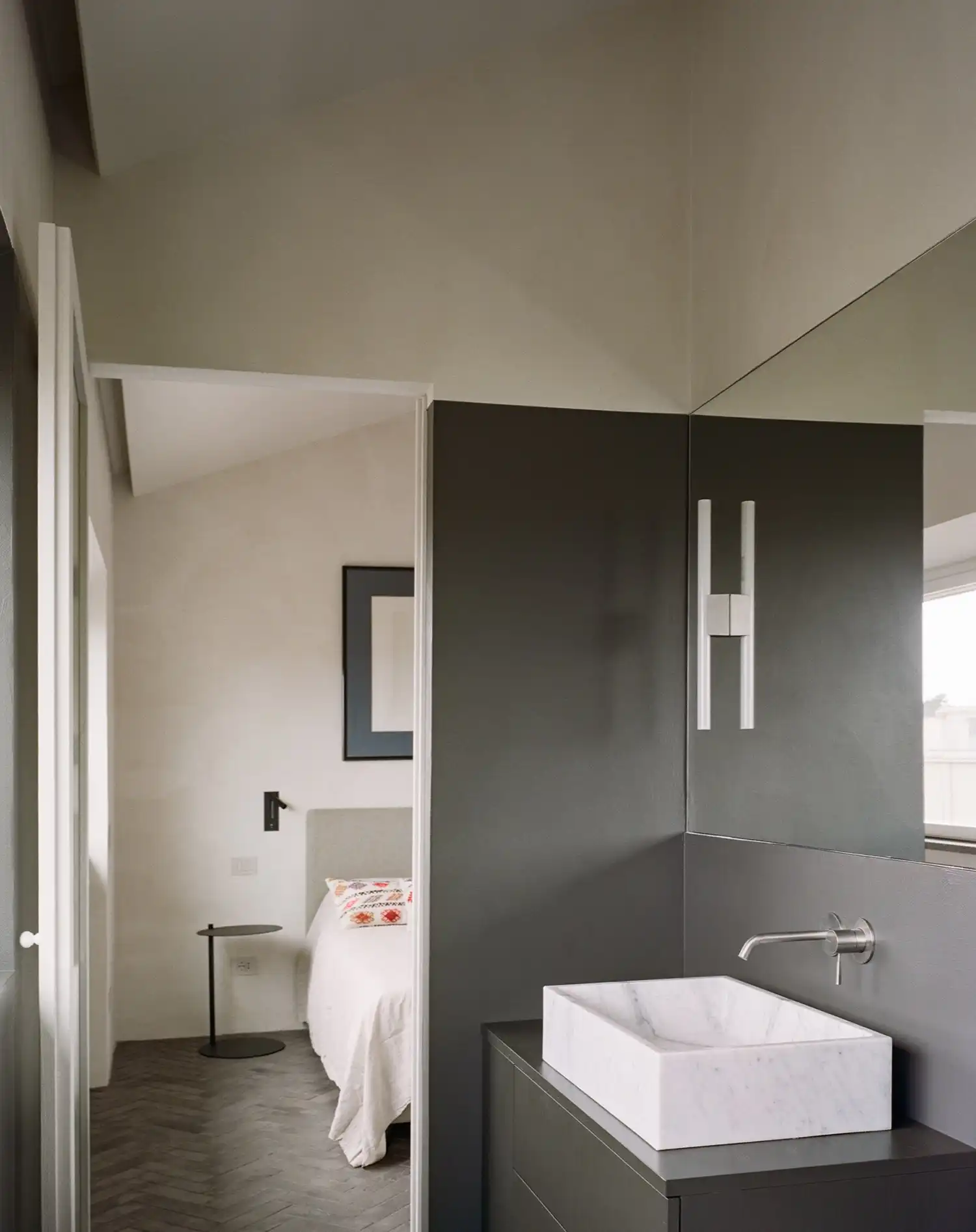 PAROS Architettura Redefines Roman Elegance with Casa ANCE’s Hybrid Guesthouse-Meeting SpaceIn Rome’s historic neighborhood near Villa Torlonia, PAROS architettura has transformed a disjointed early 20th-century penthouse into Casa ANCE - a sophisticated hybrid space that effortlessly blends residential comfort with professional functionality. The project, commissioned by Italy’s national association of building companies, reimagines the 140-square-meter apartment and its 160-square-meter terrace as both a guest residence and meeting venue, creating a compelling case study in adaptive reuse. The original layout presented significant challenges - three separate units with a complex pitched roof structure and varying ceiling heights created a fragmented interior. PAROS architettura’s solution was to completely rework the spatial organization, establishing a clear distinction between public reception areas and private zones while preserving the building’s historic character. The design team saw opportunity in the existing architectural constraints, using them to inform a thoughtful, contemporary intervention. At the heart of the renovation is a stunning open-plan public area where the original roof beams remain exposed, creating visual drama and a sense of continuity. A sliding iron-and-glass partition system provides flexible division of space, allowing the dining and meeting area to be either incorporated into the main flow or closed off for private functions. This innovative approach maintains spatial fluidity while accommodating different uses. The material palette speaks to the building’s industrial heritage while achieving modern elegance. Raw stone surfaces, microcement floors, and custom-designed wood-and-iron furnishings create a tactile, minimalist aesthetic. PAROS architettura’s careful selection of natural materials reflects both the client’s identity in the construction industry and Rome’s architectural legacy, resulting in spaces that feel simultaneously contemporary and timeless.