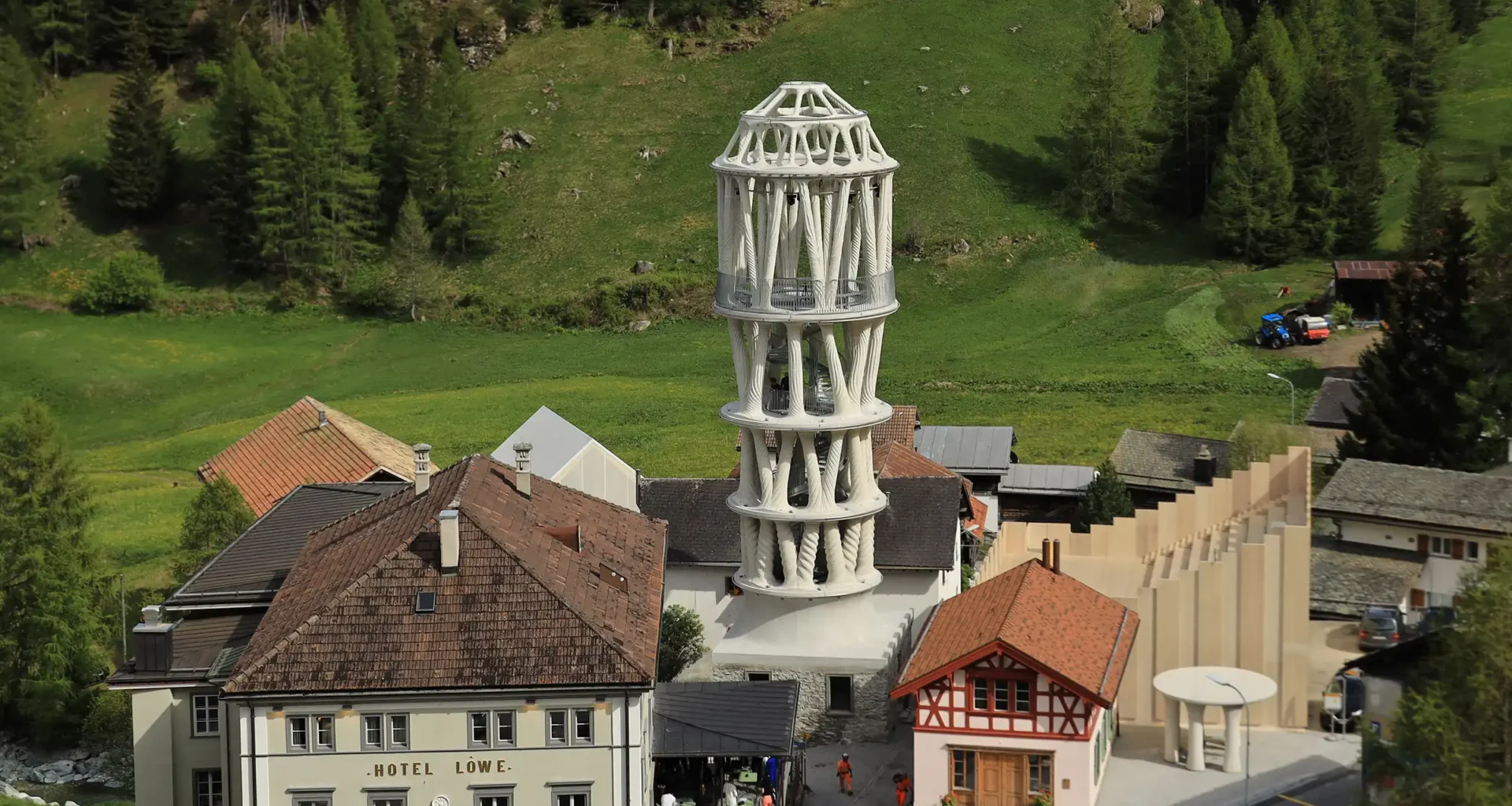 A towering 12-meter-high 3D-printed white concrete structure (Tor Alva) with intricate lattice-like patterns, standing against a Swiss alpine landscape in Mulegns.