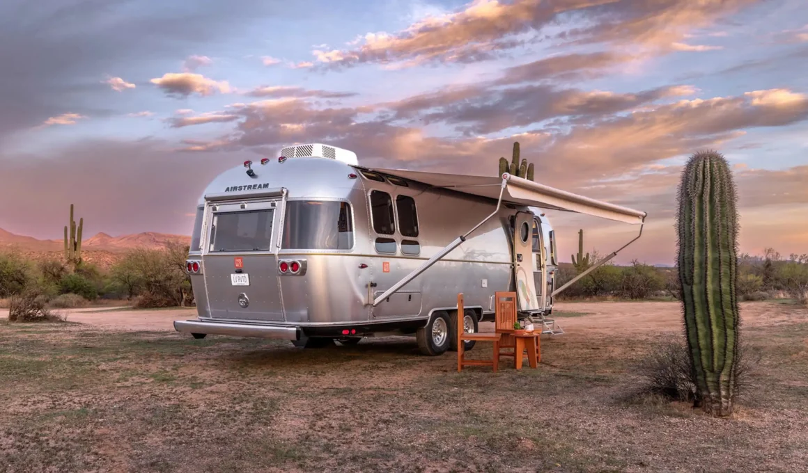 Exterior side view of the Airstream Frank Lloyd Wright Usonian Travel Trailer with sleek aluminum shell and signature Cherokee Red accents, parked in a natural landscape.