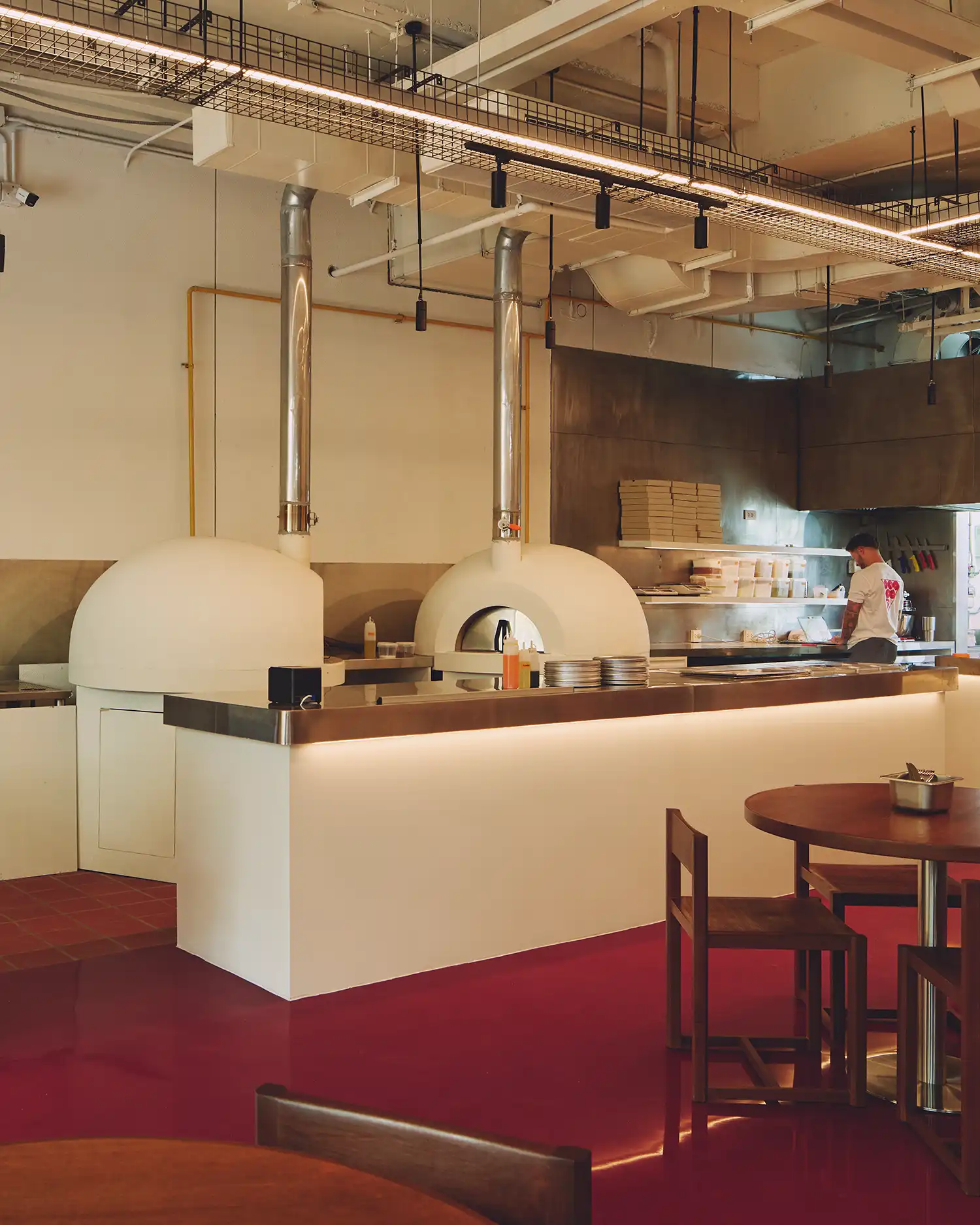 Twin white plaster pizza ovens at PI SHOP Bangkok, with passata-red seating and glossy epoxy floors.