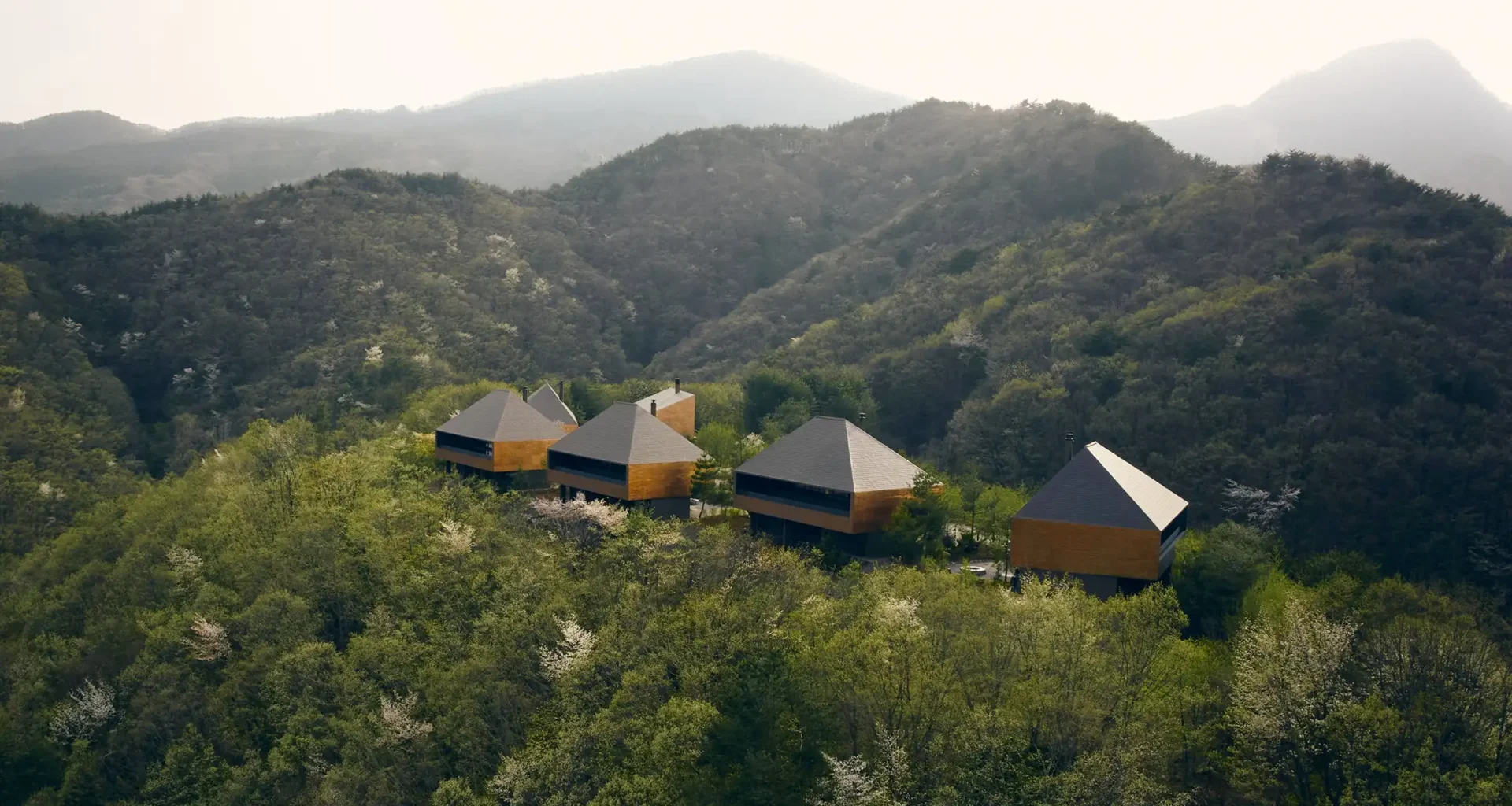 Aerial view of five copper-clad luxury villas by Suppose Design Office perched on Minakami mountain, Japan, overlooking dramatic valley with seasonal landscapes and private infinity pools.