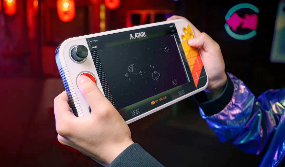 Atari Gamestation Go retro handheld console showing orange and yellow design with tactile buttons, trackball, and paddle controller.