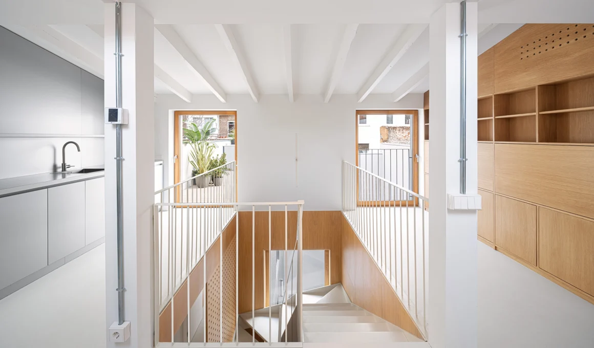 Open-plan kitchen in Casa Castelar, Madrid, by Solar Arquitectura, featuring custom cabinetry, a central island, and views to the courtyard through the perforated recycled aluminium facade.
