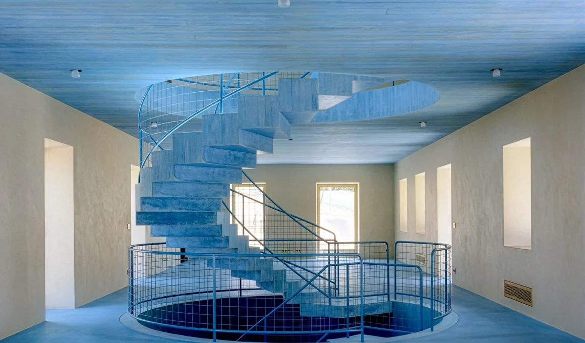 A sculptural, light blue helical concrete staircase ascends through a void, illuminated by a skylight in a historic Sintra quinta house renovated by Arquitectura-G.