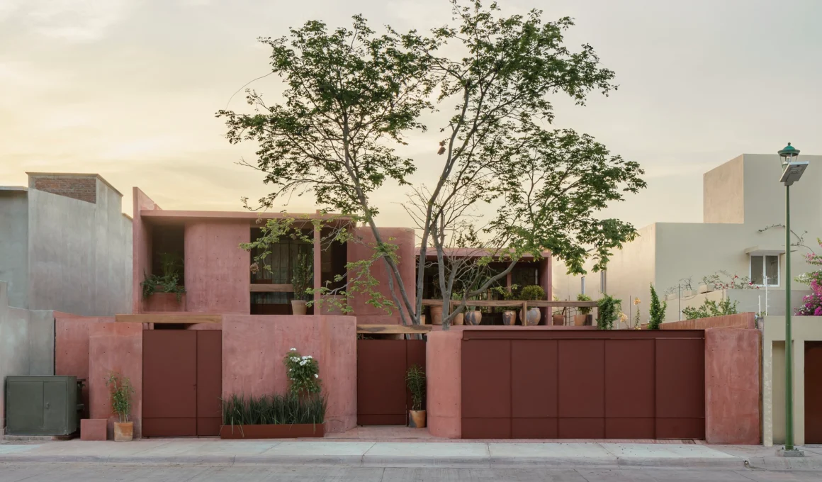 Curb view of Casa Roja in Bahías de Huatulco, showcasing its geometric red pigmented concrete facade, local brick, and shaded openings.