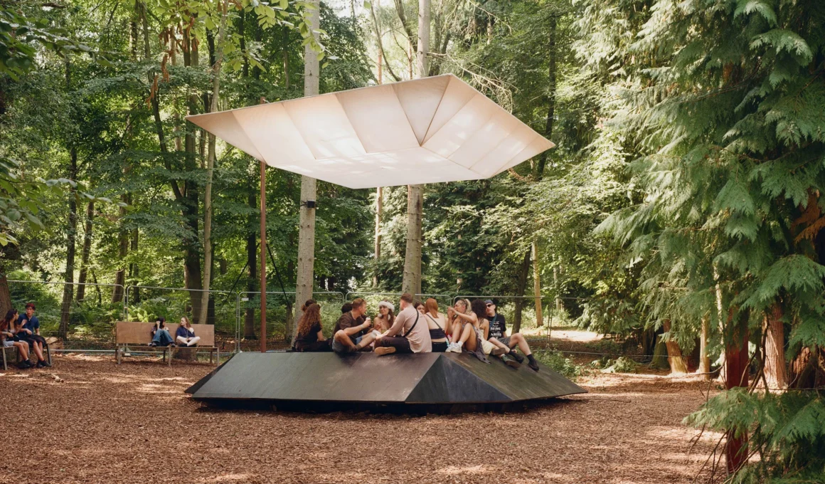 EBBA Architects Pulse installation night view, showing the glowing, colourful canopy suspended over the black seating platform in the Houghton Festival woodland clearing.