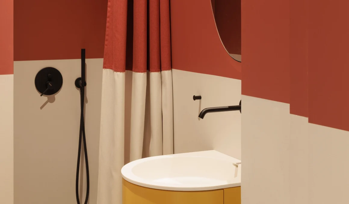 Modern color-blocked bathroom with terracotta and cream epoxy walls, black fixtures, and a yellow resin vanity in a minimalist design.