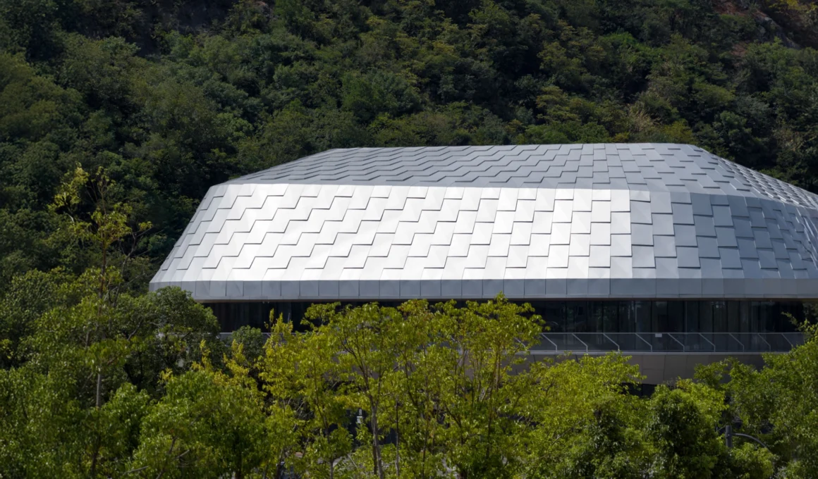 Hushan Sports Park Swimming Center by LYCS Architecture, a fluid concrete and glass structure nestled within the verdant landscape of Tiger Mountain in Jiangshan, China.