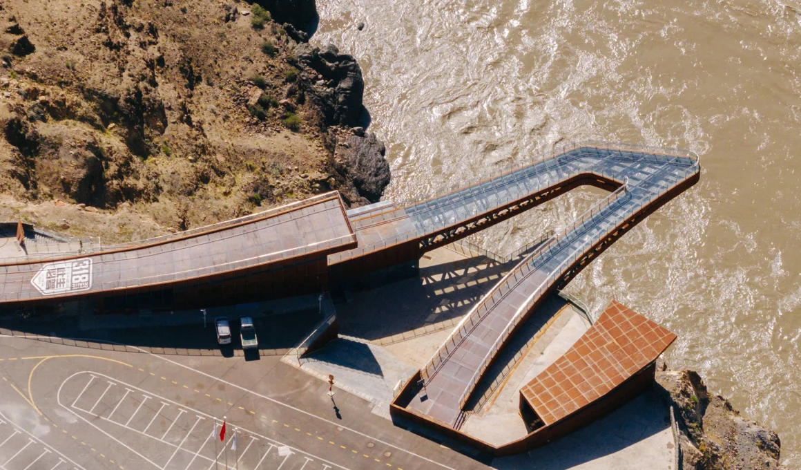 A dramatic aerial view of the cantilevered Nujiang River 72 Turns glass viewing platform by Archermit, a red steel structure extending over the deep canyon of the Sichuan-Tibet Highway in Tibet.