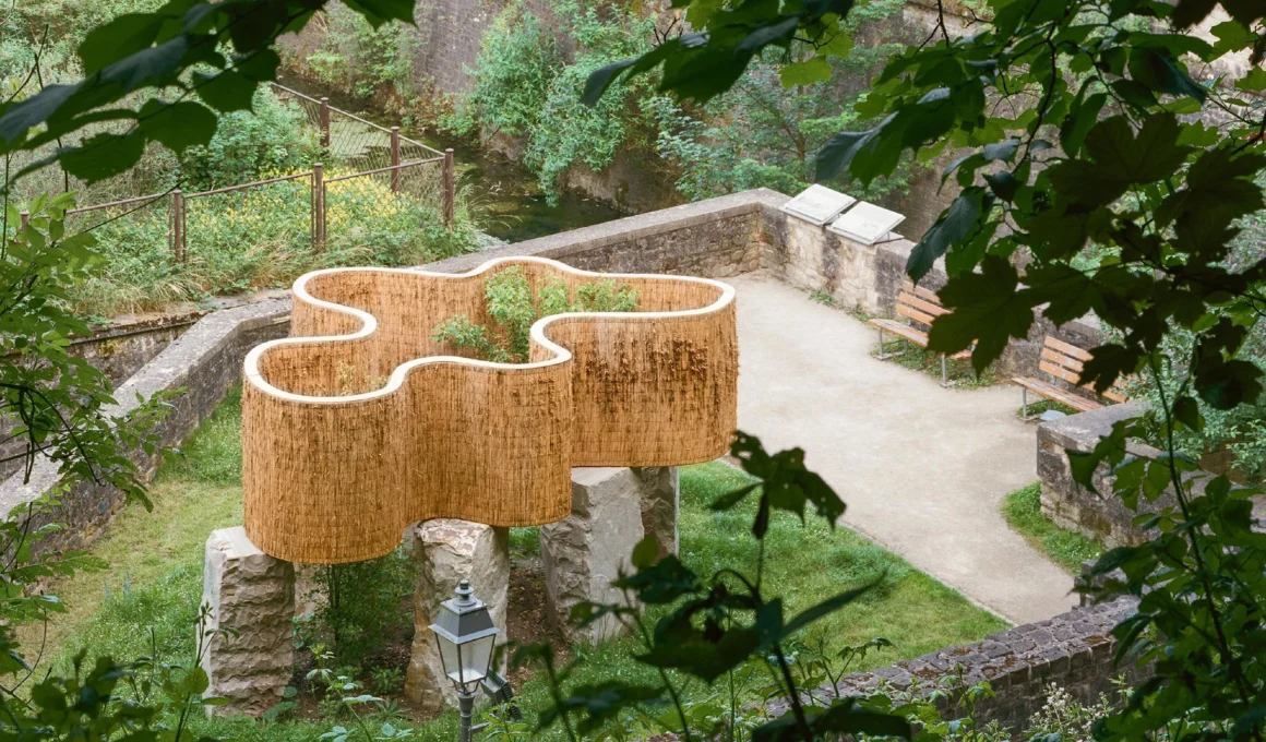 Atelier Faber Solum installation in Luxembourg City featuring layered reeds atop Luxembourg sandstone pillars, illustrating soil permeability and ecological design for water management.