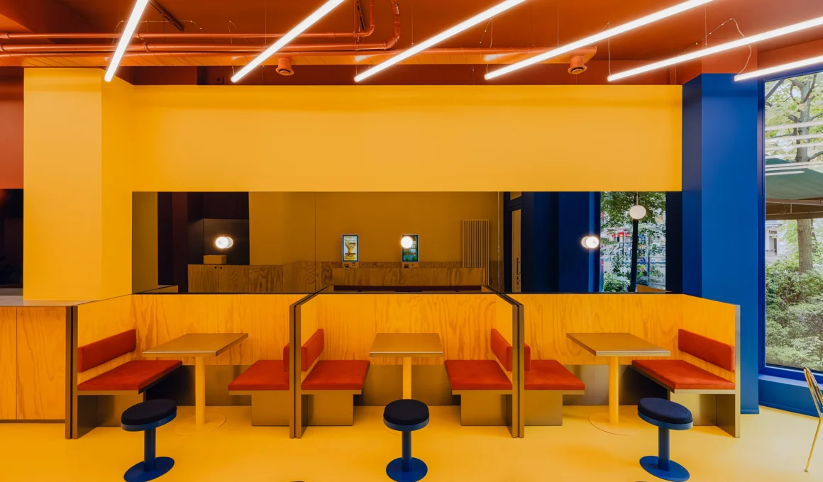 Bruzkus Greenberg FLIP-N-FRY Berlin restaurant interior design with bold yellow colour-blocking, stainless steel banquettes, and terra-cotta accents.
