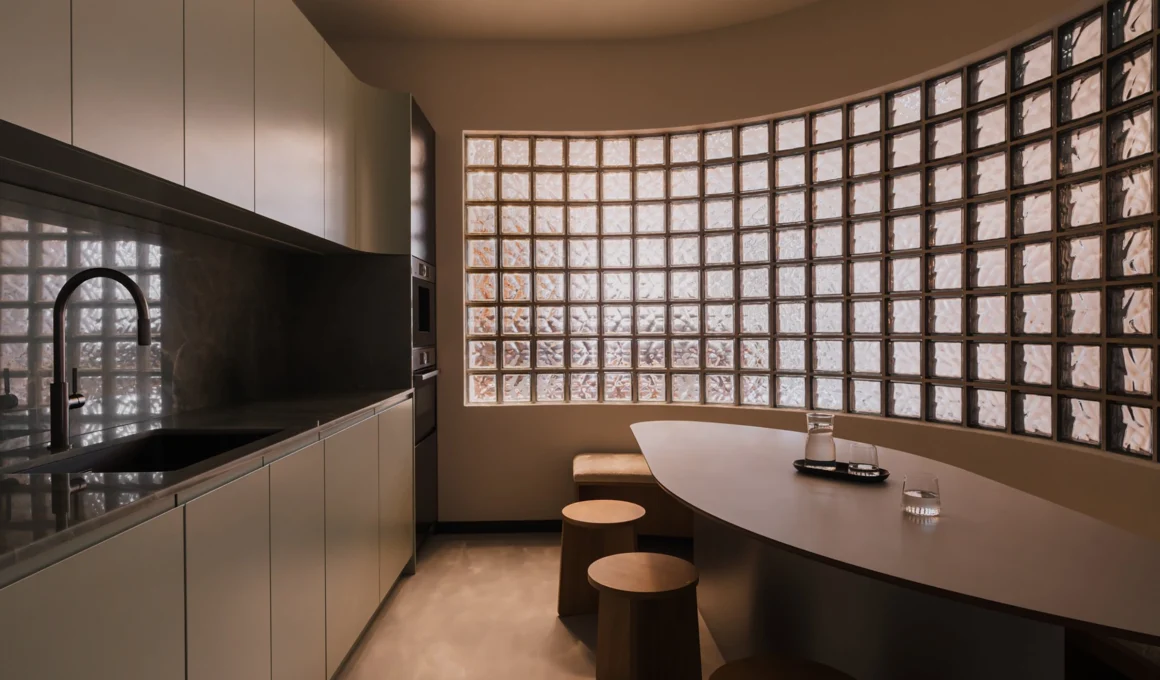 Deep light penetration urban kitchen with a curved glass brick wall maximizing natural light diffusion.