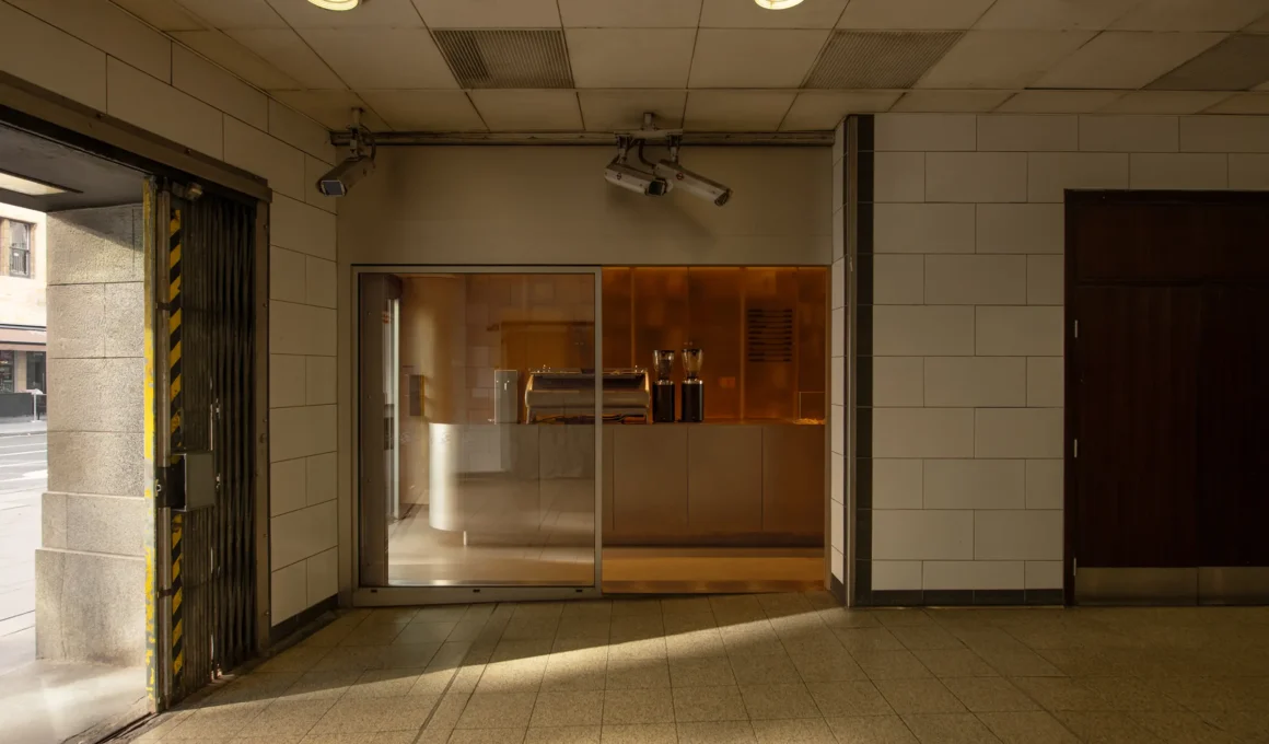 EBBA's Espresso Bar interior in Holborn London, featuring a minimalist dark timber monolithic counter, soft lighting, and white ceramic tile wall design at the London tube station entrance.