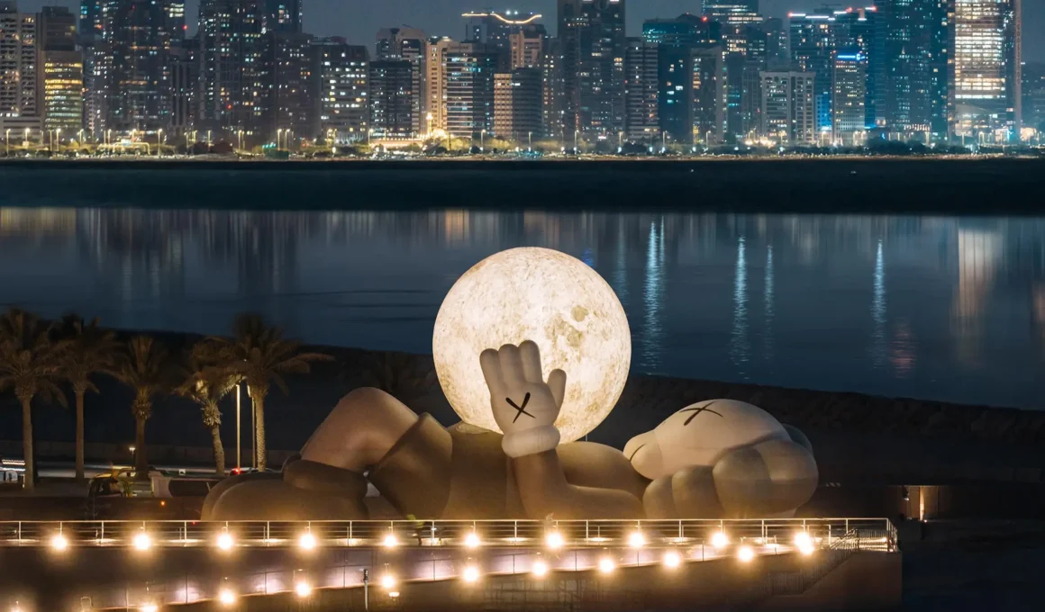 32-meter KAWS Companion inflatable art installation holding glowing moon on Abu Dhabi Mina Zayed waterfront.