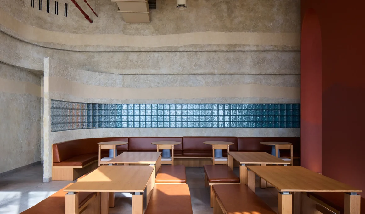 KIDZ Studio Blu Pizzeria Abu Dhabi interior showing turquoise curved glass block walls, monumental plaster forms, and central open kitchen.